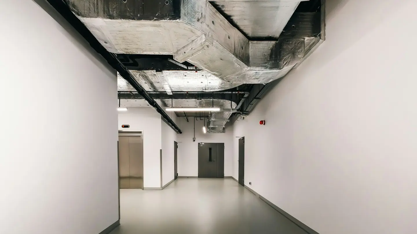 Long institutional corridor with exposed services and controlled doors